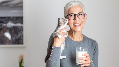 une femme aux cheveux blancs tient un chaton et un verre de lait